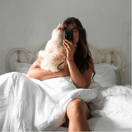 Woman sitting on bed with bamboo sheets, demonstrating pet hair repellent fabric.