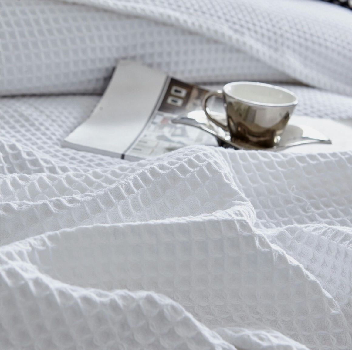 Bamboo waffle throw blanket in white, displayed on a cozy bed with a cup of coffee and a magazine nearby