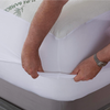 Close-up of a person fitting a white sheet over Adorearth's Pure Bamboo mattress topper, highlighting the product's snug fit and quality fabric.