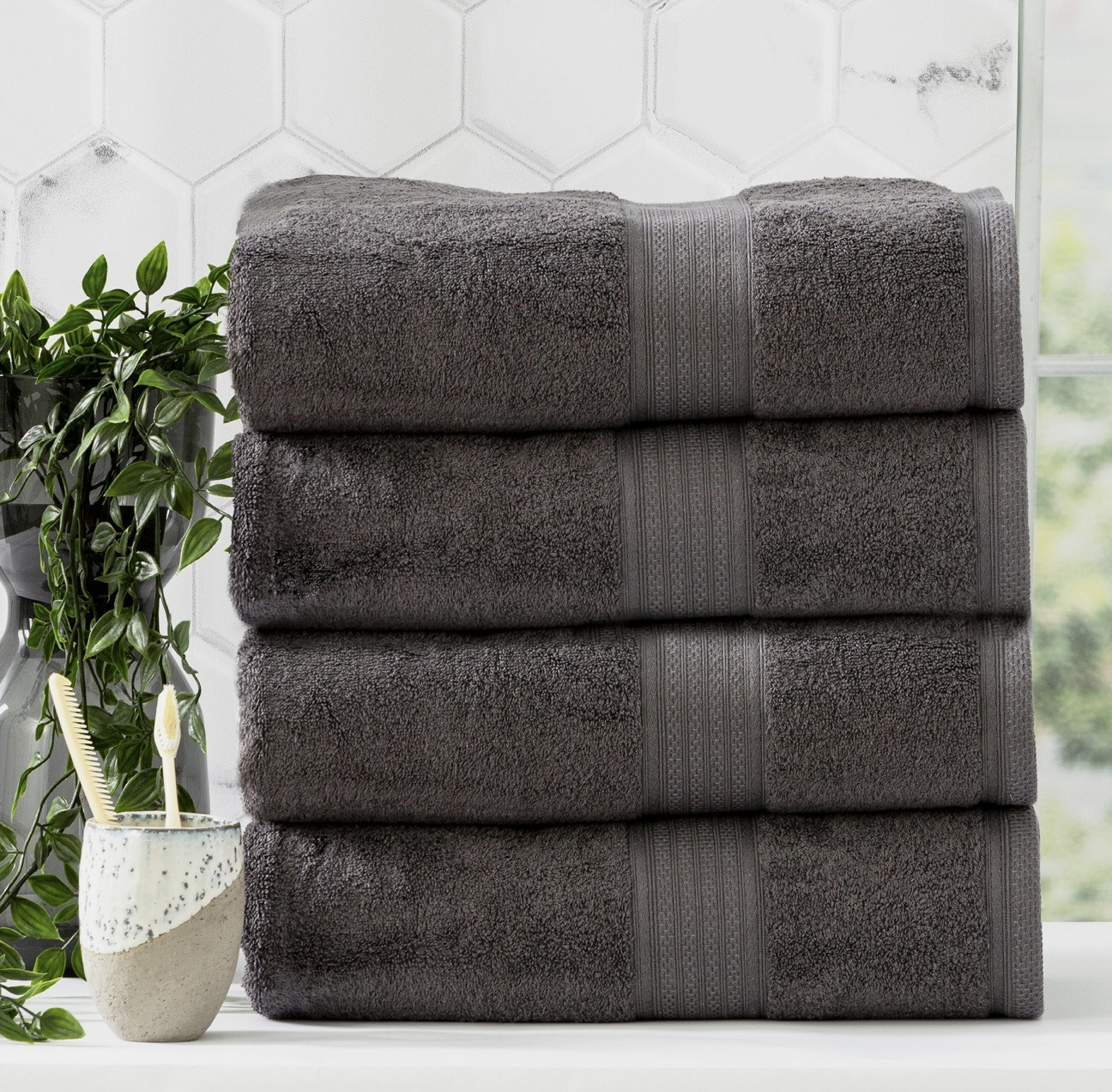 Stack of dark gray Bamboo Towels with decorative stripes, neatly arranged on a white surface beside a plant