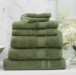 Stack of greenBamboo Towels arranged neatly, with a small white flower vase and a hexagonal tile wall in the background.