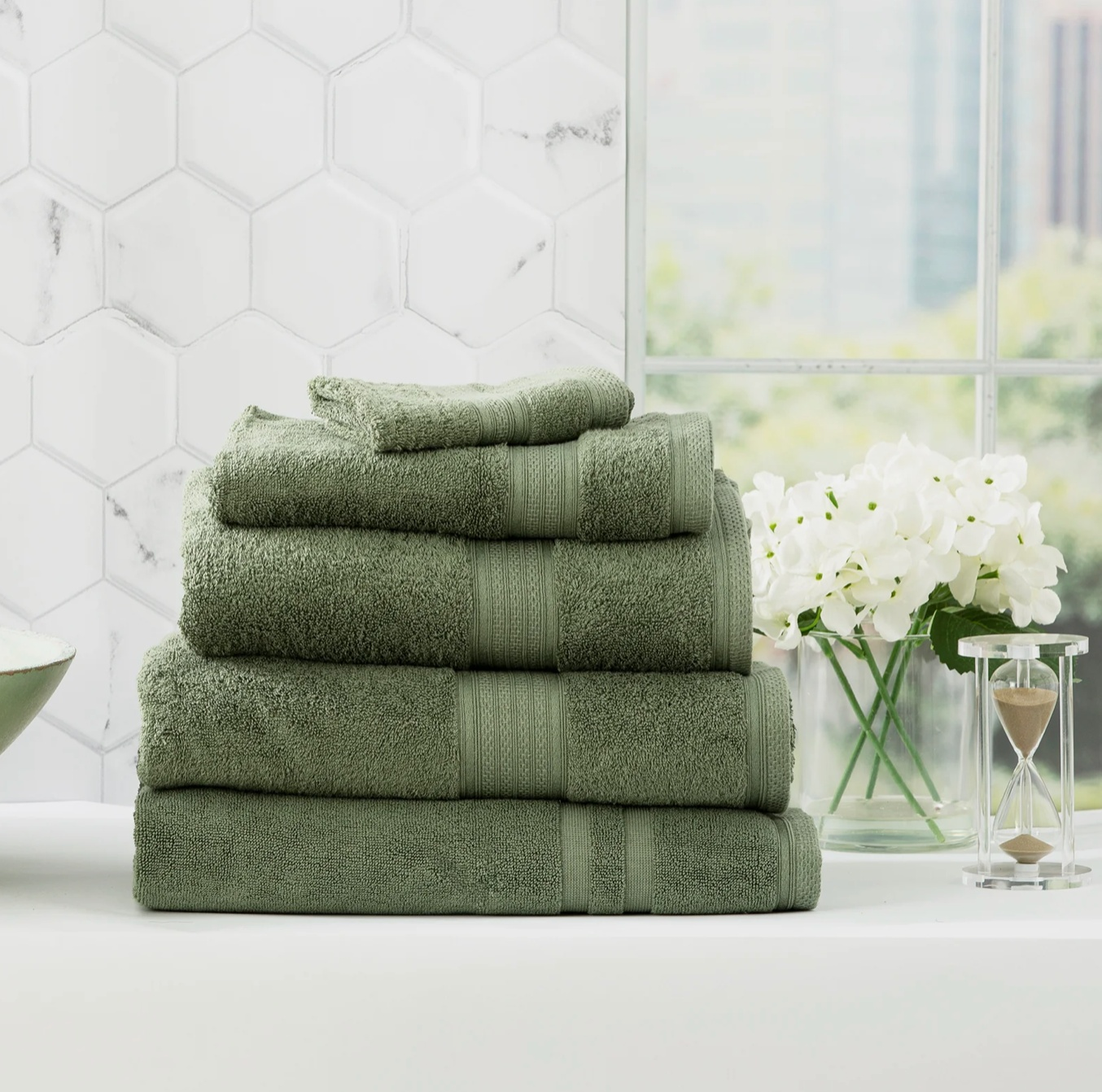 Stack of green Adorearth™ organic bamboo towels on a bathroom counter with white flowers in the background