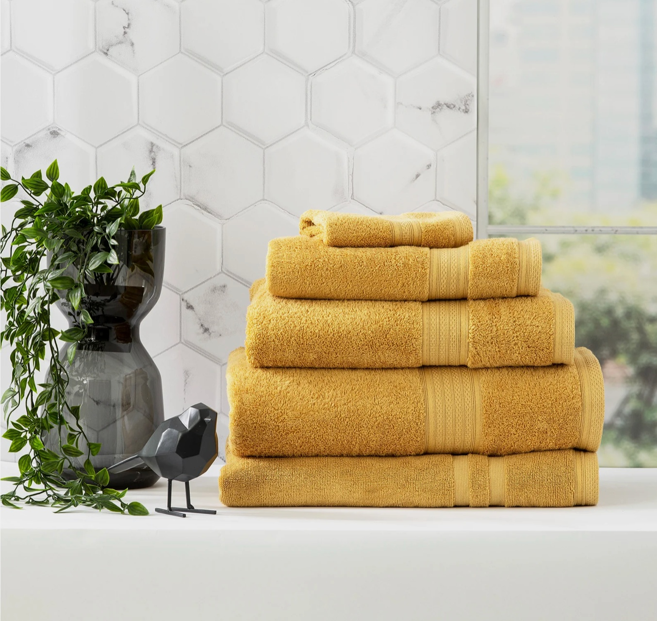 Stack of Adorearth™ organic bamboo towels in yellow on a bathroom counter with a plant and decorative black bird.