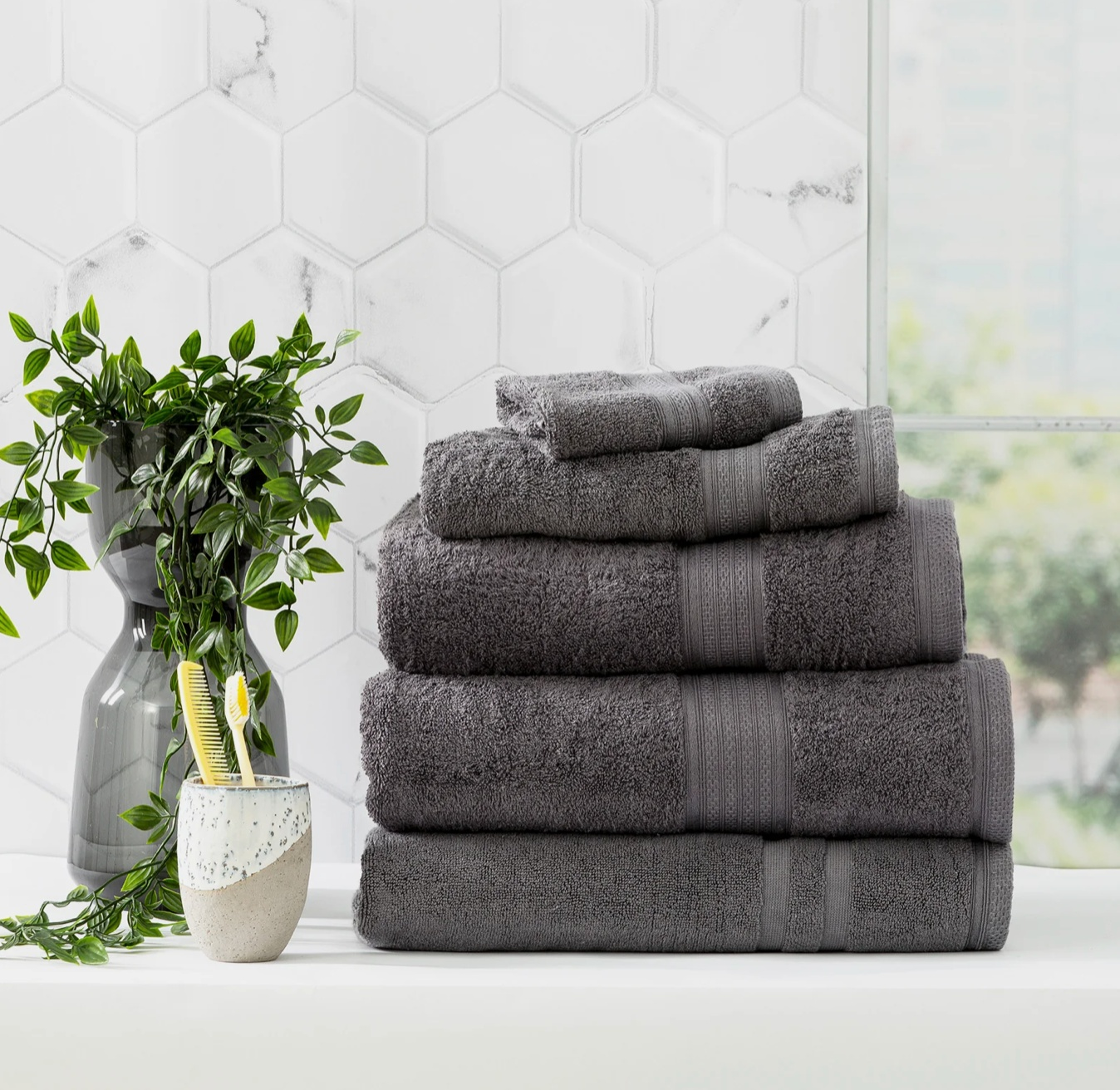 Stack of Adorearth™ organic bamboo towels in a bathroom setting with a potted plant and toothbrush holder on the side.